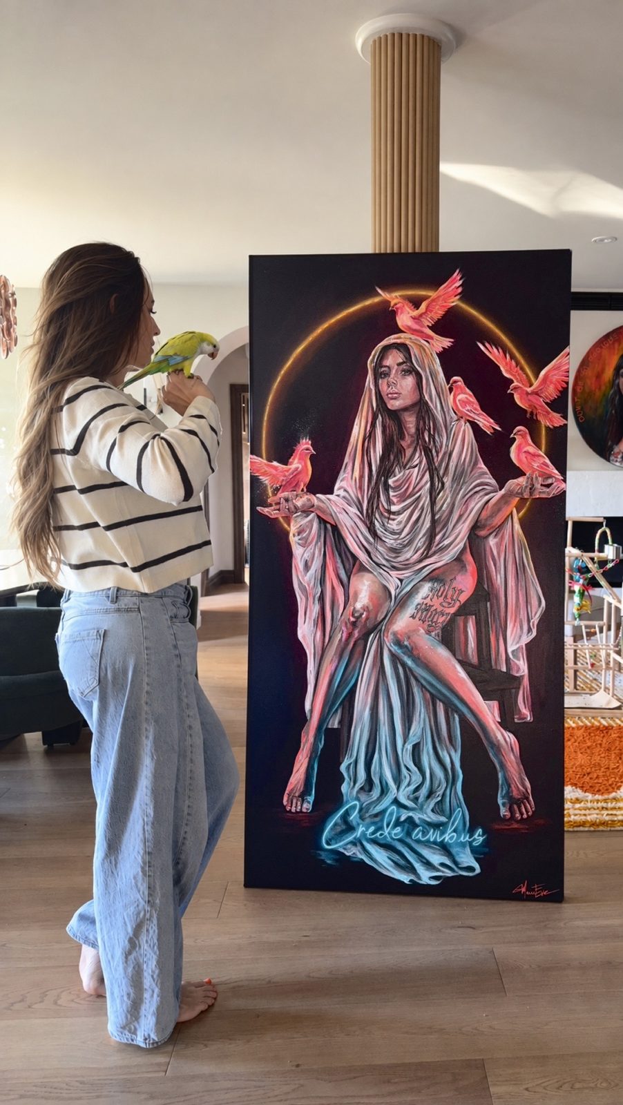 Marie-Ève, sa perruche Sunny sur la main, devant la toile Holy Mary